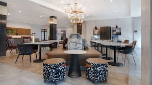 A modern hotel lobby with a central seating area, multiple tables, and a chandelier. - Home2 Suites by Hilton Anderson Downtown (Anderson)