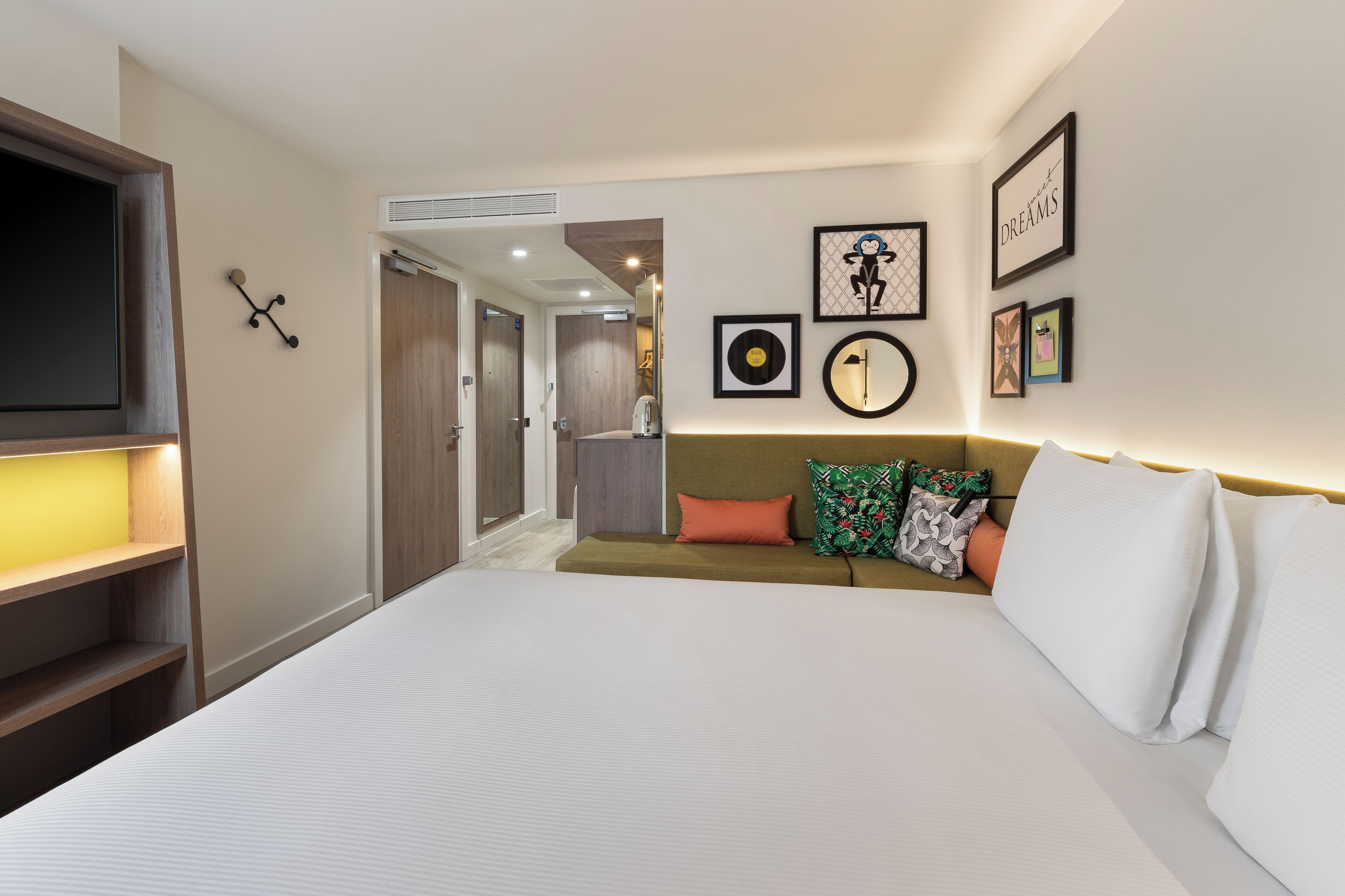 A hotel room with a large bed, a TV, a wardrobe, and a hallway leading to another room.