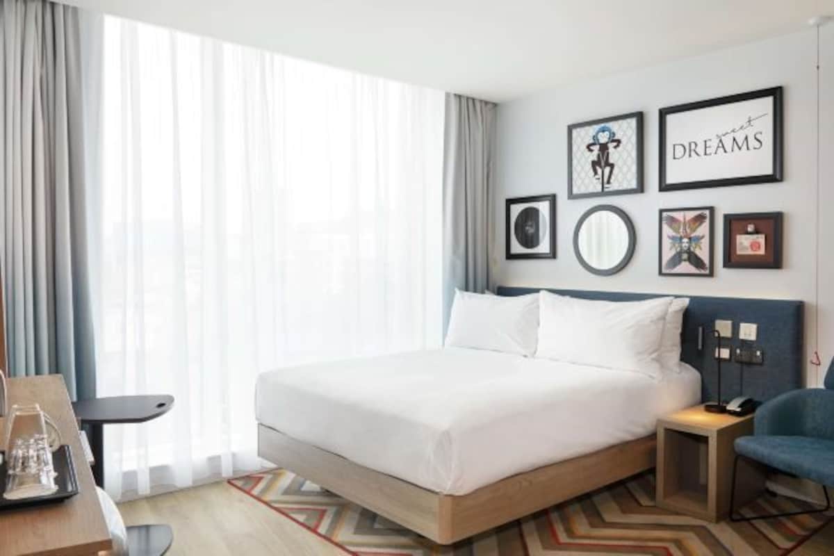 A hotel room with a large bed, a desk, a chair, and a window with curtains.