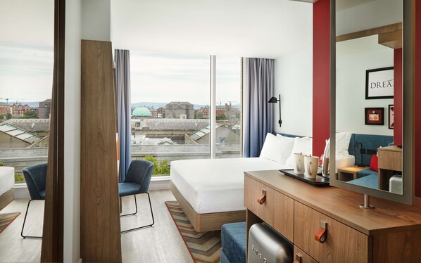 A modern hotel room with a large bed, a desk with a computer, a chair, and a view of the cityscape. - Hampton by Hilton Dublin City Centre (Dublin)