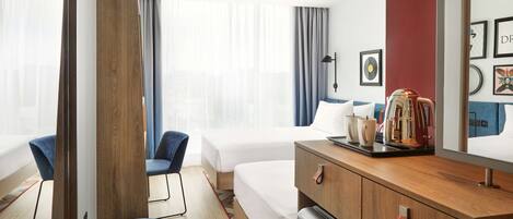 Una habitación de hotel con una cama, un escritorio con cafetera, una silla y un aparador.