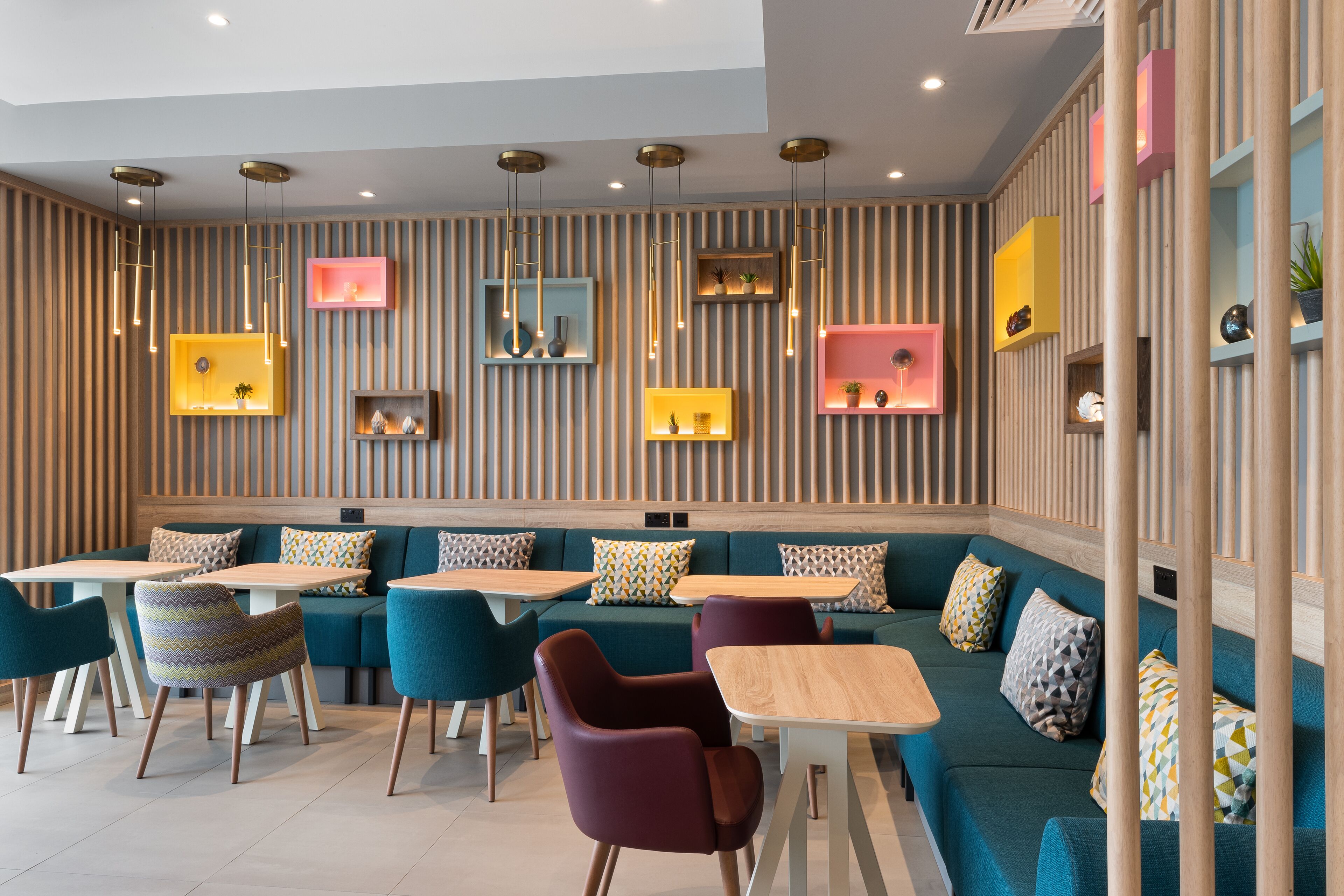 A modern interior with a sectional sofa, dining tables, and chairs, featuring a striped wall and pendant lighting.