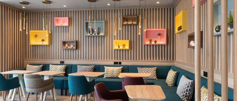Un interior moderno con sofá modular, mesas de comedor y sillas, que presenta una pared a rayas e iluminación colgante.