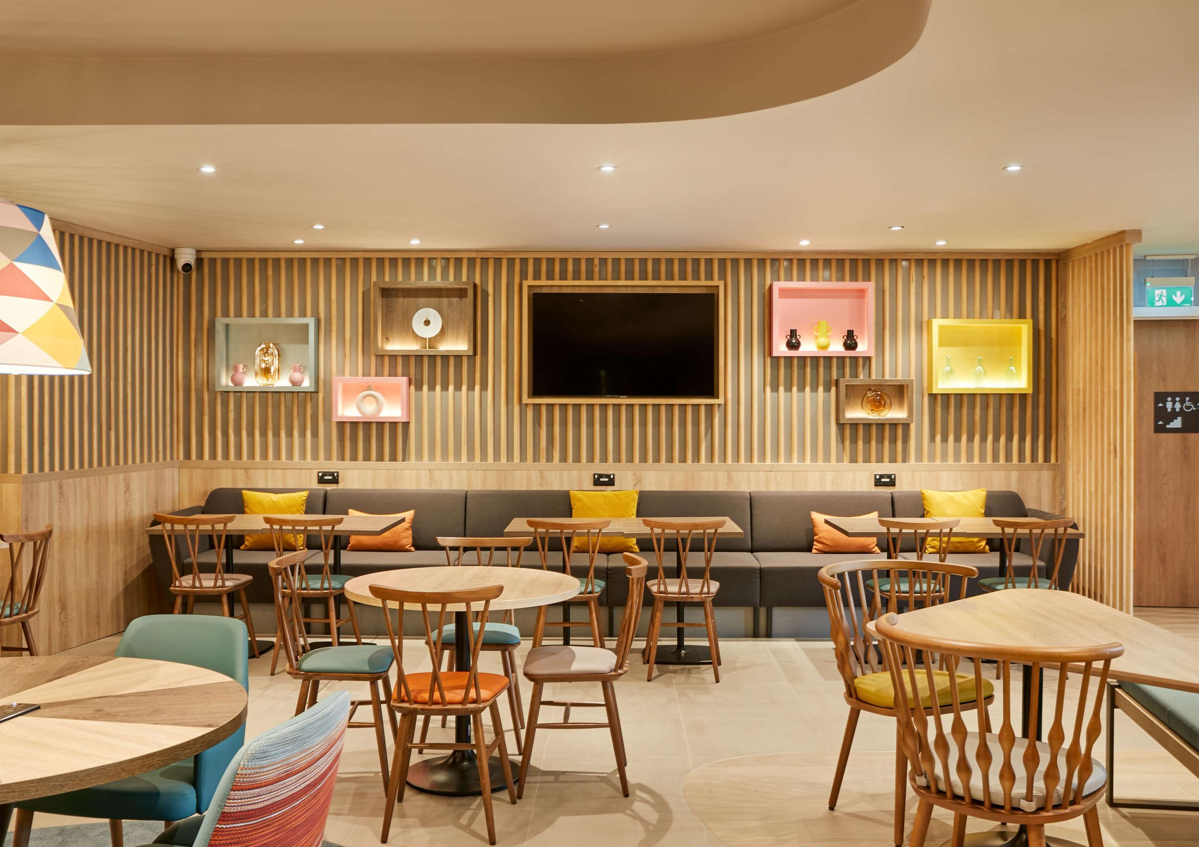 A modern restaurant with wooden panel walls, round tables, and cushioned seating.