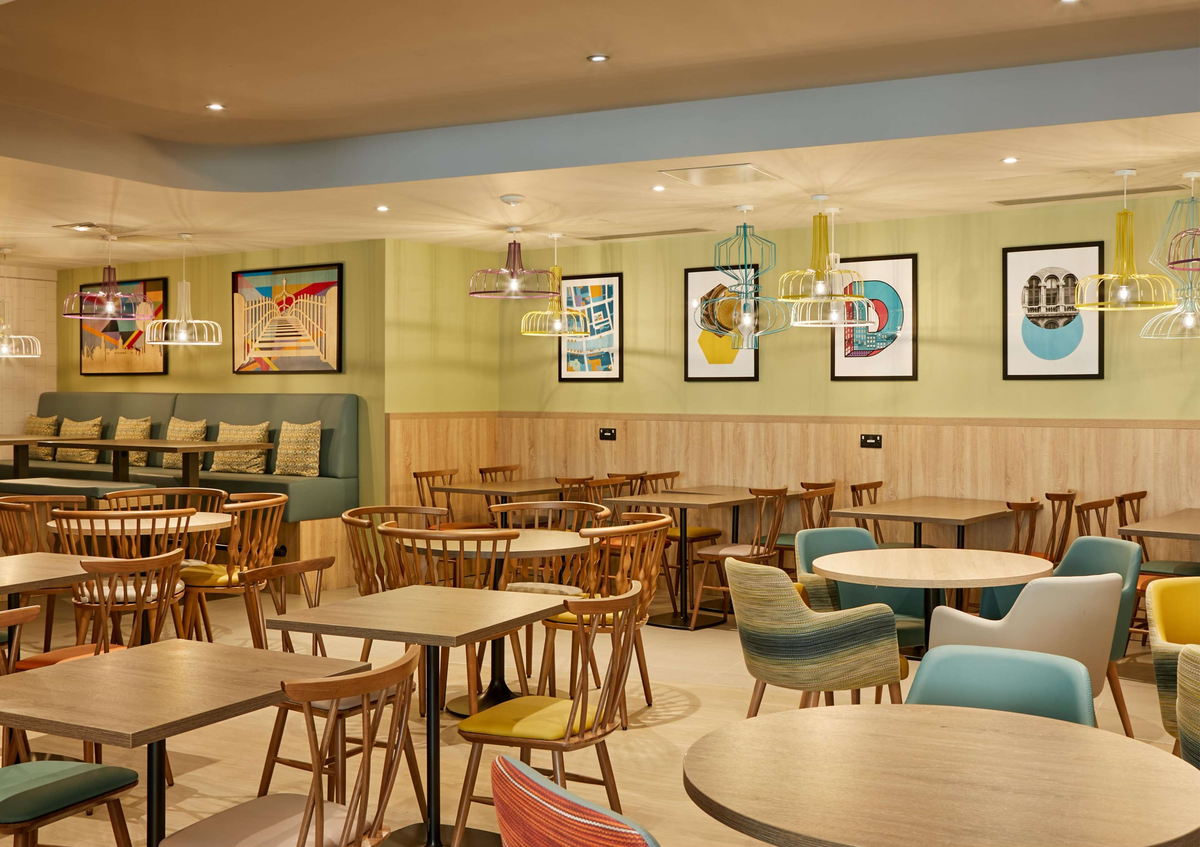 A restaurant with wooden tables and chairs, a green sofa, and colorful artwork on the walls.