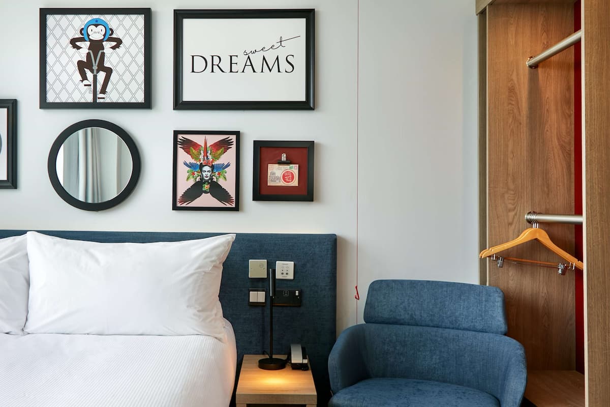 A hotel room with a bed, a chair, a nightstand, and wall art including a framed 'DREAMS' sign and a framed picture of a monkey.
