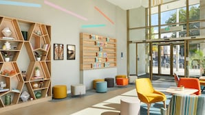 A modern lobby with a wooden bookshelf, colorful chairs, and a welcoming sign. - Hampton by Hilton Dublin City Centre (Dublin)