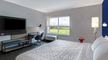 A hotel room with a large bed, a desk with a chair, a flat-screen TV, a window with a view of the outdoors, and a bedside lamp.