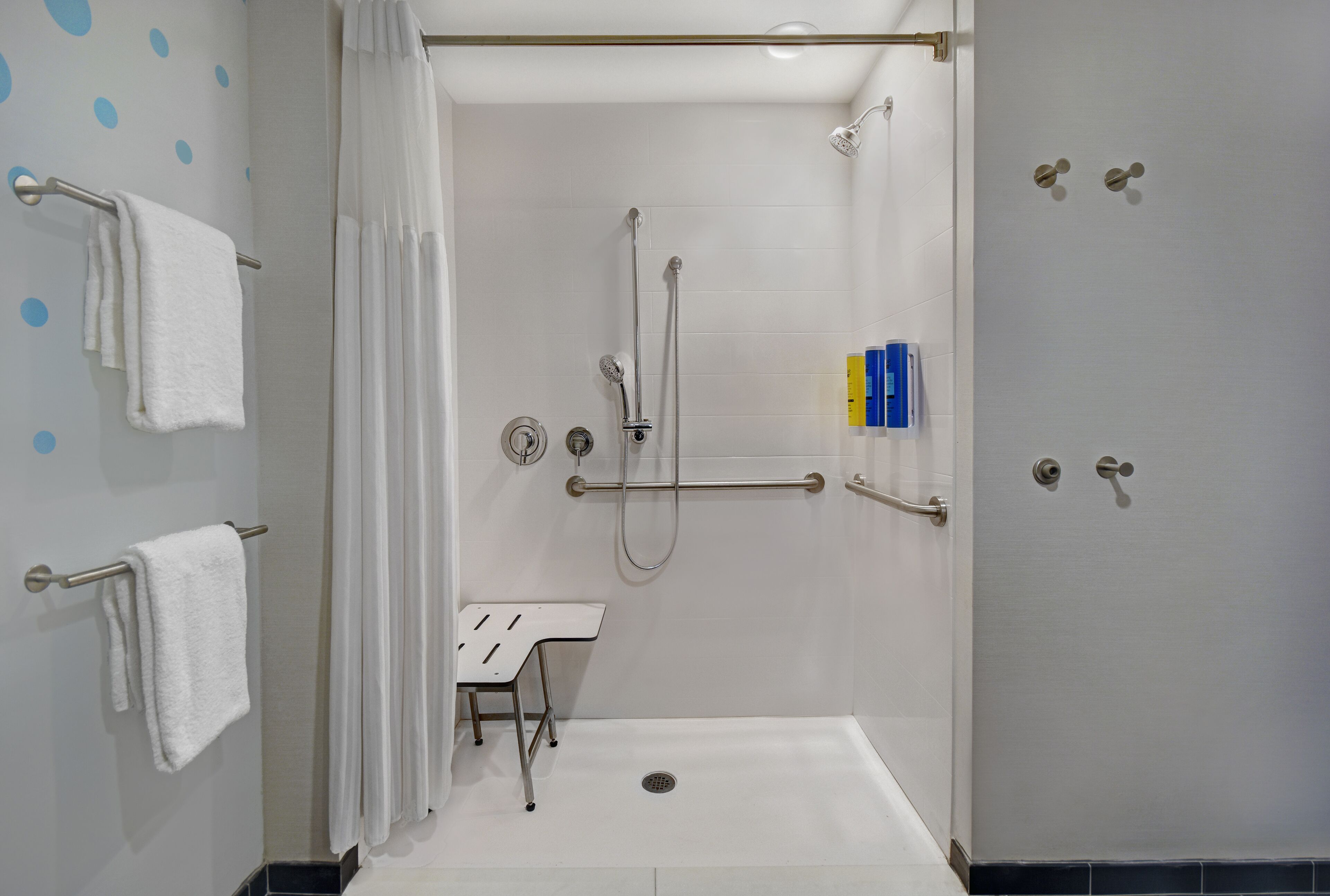 A modern bathroom with a walk-in shower, grab bars, a white sink, and a towel rack.