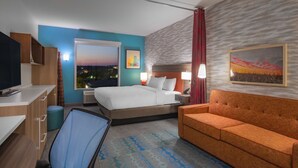 A hotel room with a bed, a sofa, a desk with a TV, and a chair. - Home2 Suites by Hilton Omaha I-80 at 72nd Street, NE (Omaha)