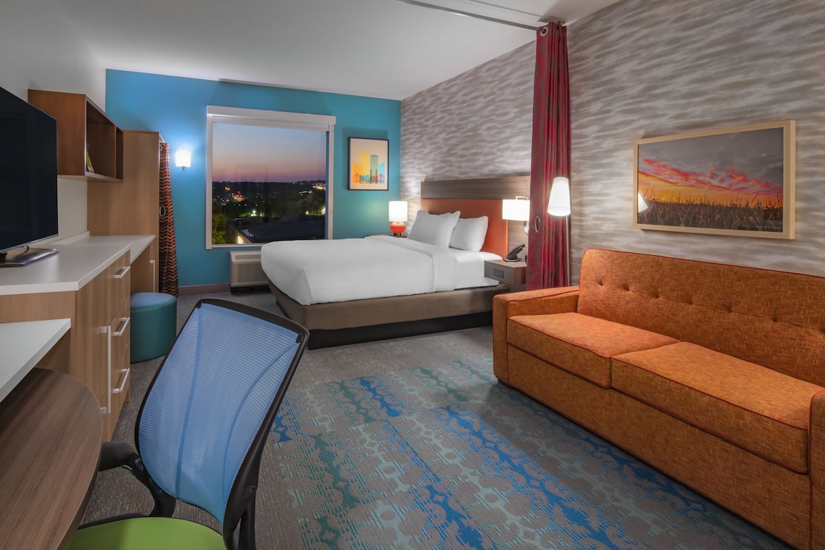 A hotel room with a bed, a sofa, a desk with a TV, and a chair.