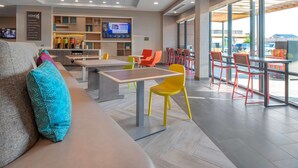 A modern hotel lobby with a seating area, a kitchen, and a large window offering a view of the parking area. - Home2 Suites by Hilton Omaha I-80 at 72nd Street, NE (Omaha)