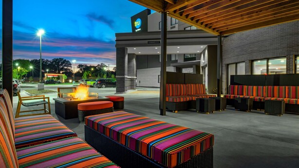 An outdoor seating area with colorful striped cushions, a fire feature, and a view of a building with a 'tru' sign. - Home2 Suites by Hilton Omaha I-80 at 72nd Street, NE (Omaha)