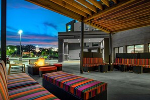 Un espace extérieur aménagé avec des coussins rayés aux couleurs vives, un foyer et une vue sur un bâtiment portant l’inscription « tru ».