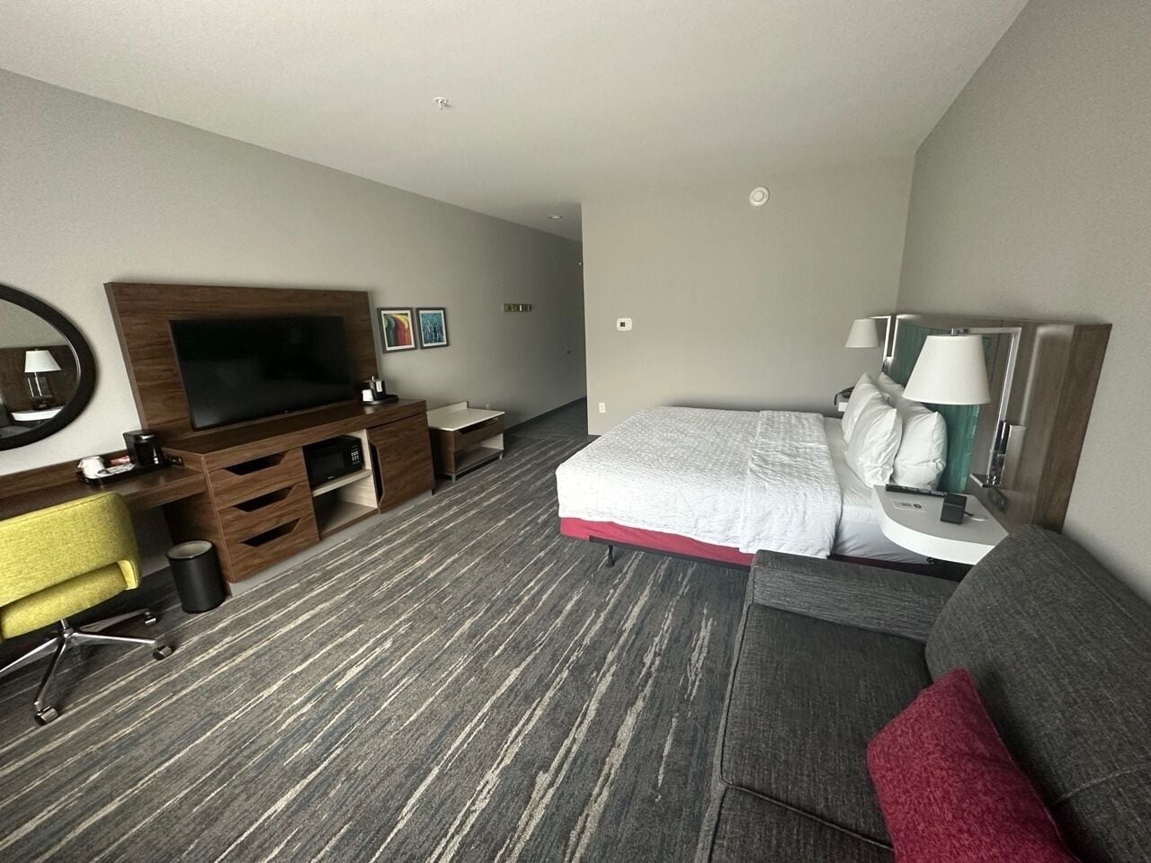 A hotel room with a bed, a desk with a chair, a TV, and a sofa.