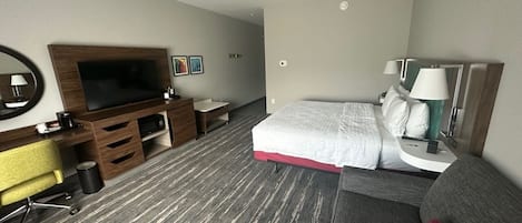 A hotel room with a bed, a desk with a chair, a TV, and a sofa.
