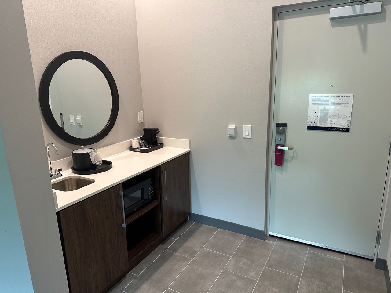Een moderne badkamer met een wastafel, spiegel en een deur met een nooduitgangsbord.