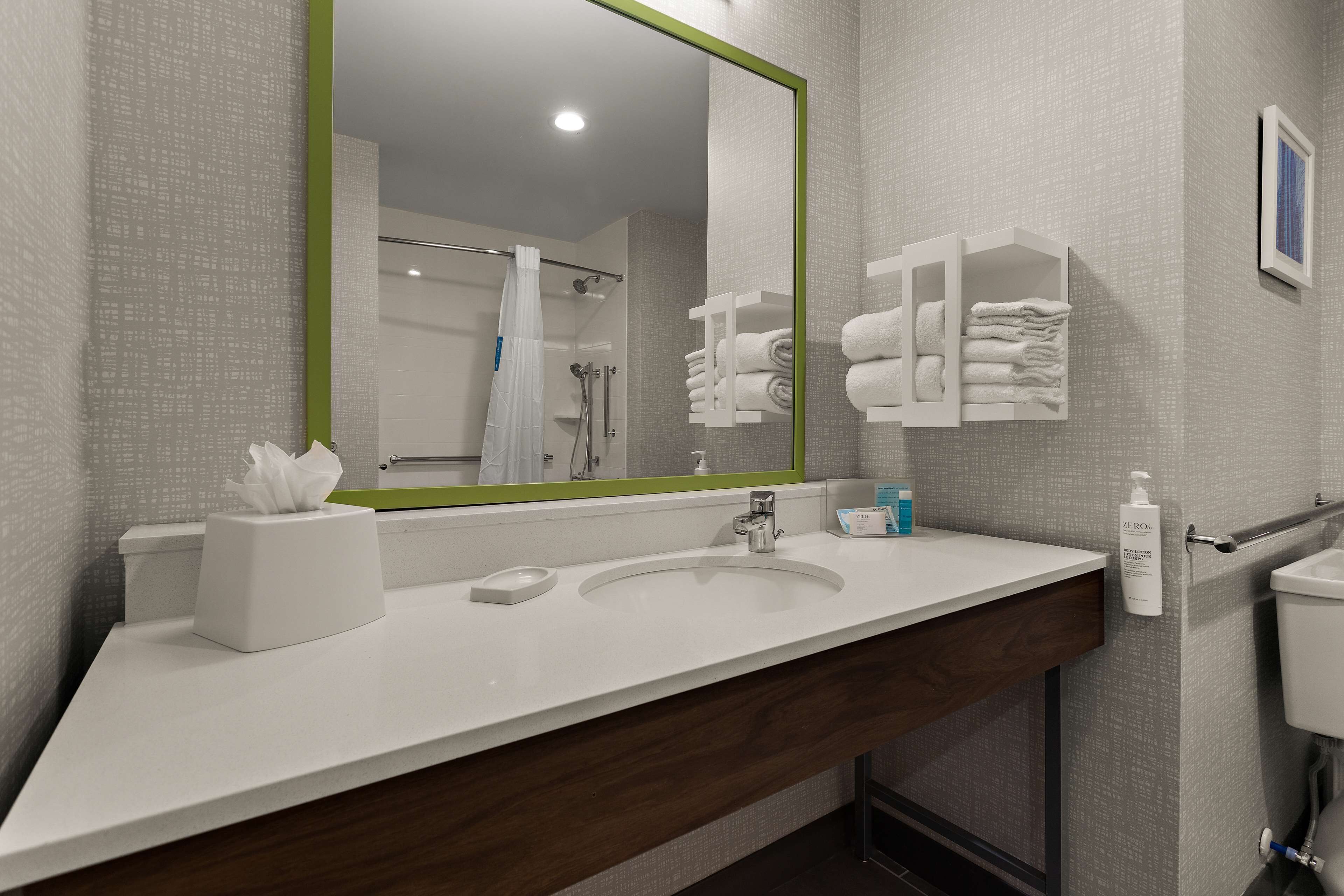 Uma casa de banho moderna com uma pia branca, um espelho com moldura verde, um porta-toalhas e uma sanita.