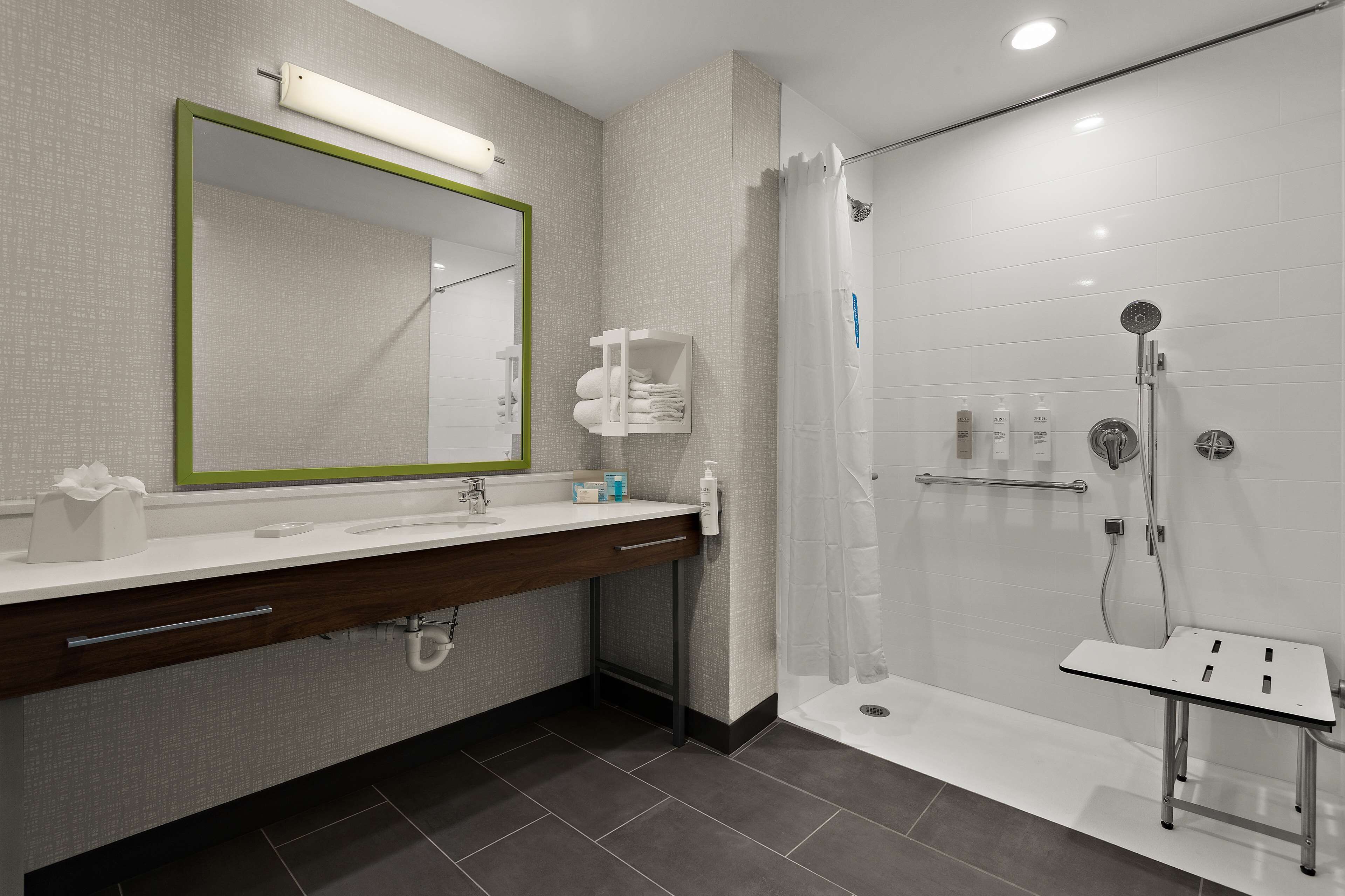 A modern bathroom with a large mirror, a sink with a towel rack, and a shower area.