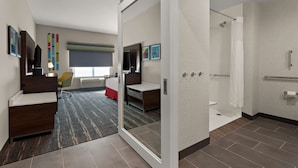 A modern hotel room with a large mirror, a desk, a chair, a bed, and a shower area. - Hampton Inn & Suites Ruskin I-75 (Ruskin)