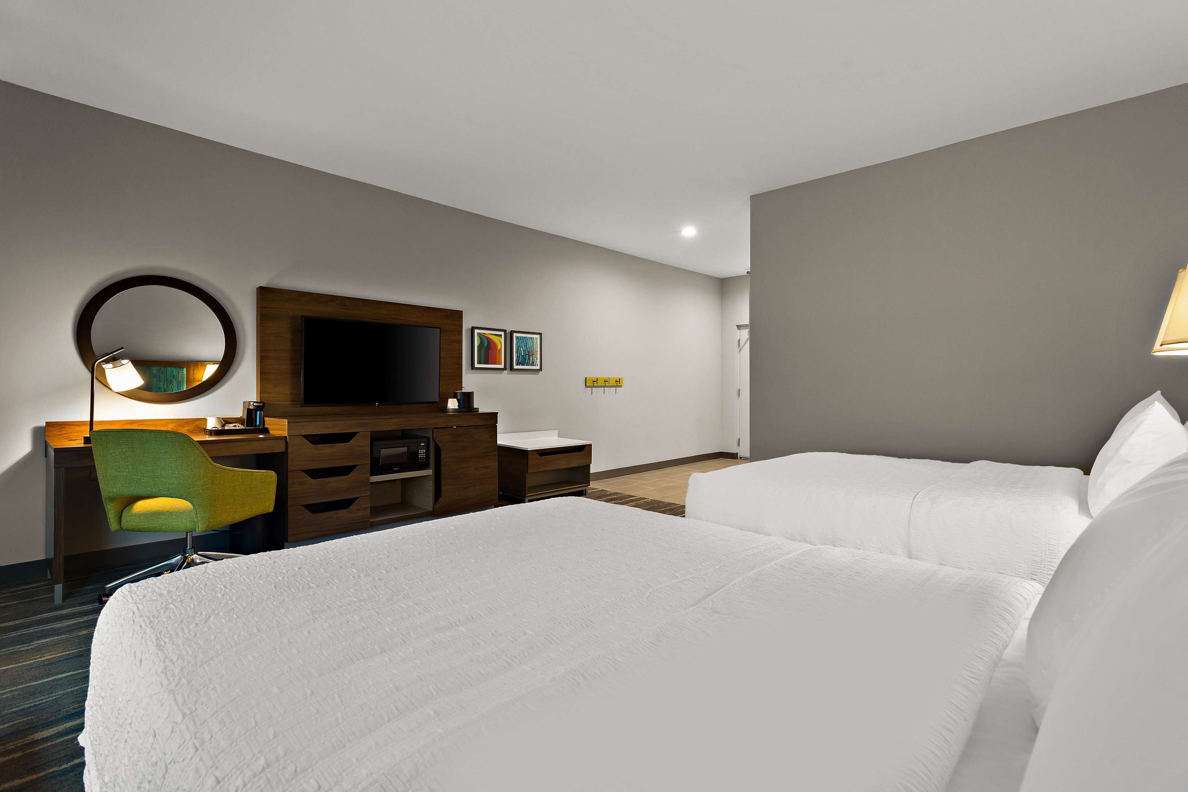 A hotel room with two beds, a desk with a chair, a TV, and a mirror.