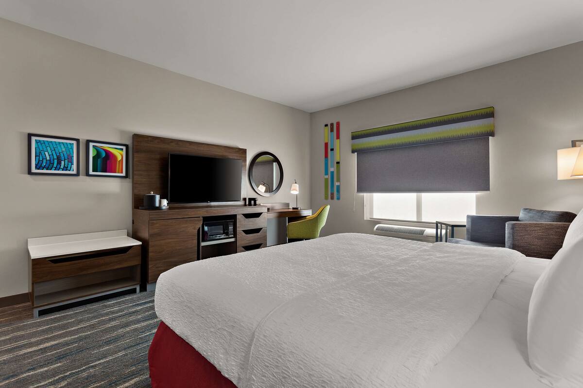 A hotel room with a large bed, a desk with a computer, a TV, a mirror, and artwork on the walls.