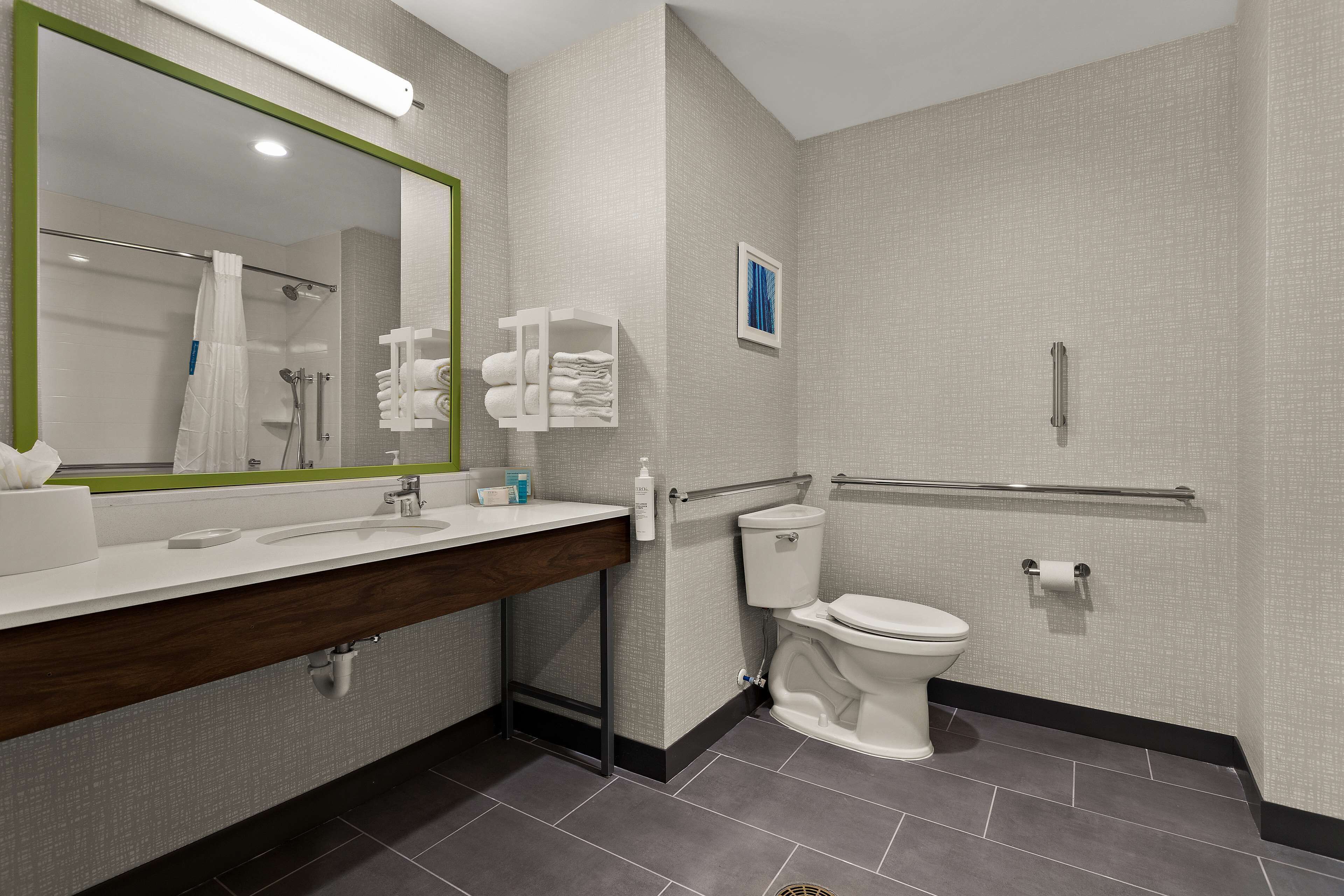 A modern bathroom with a large mirror, a toilet, a sink with a towel rack, and a shower area.