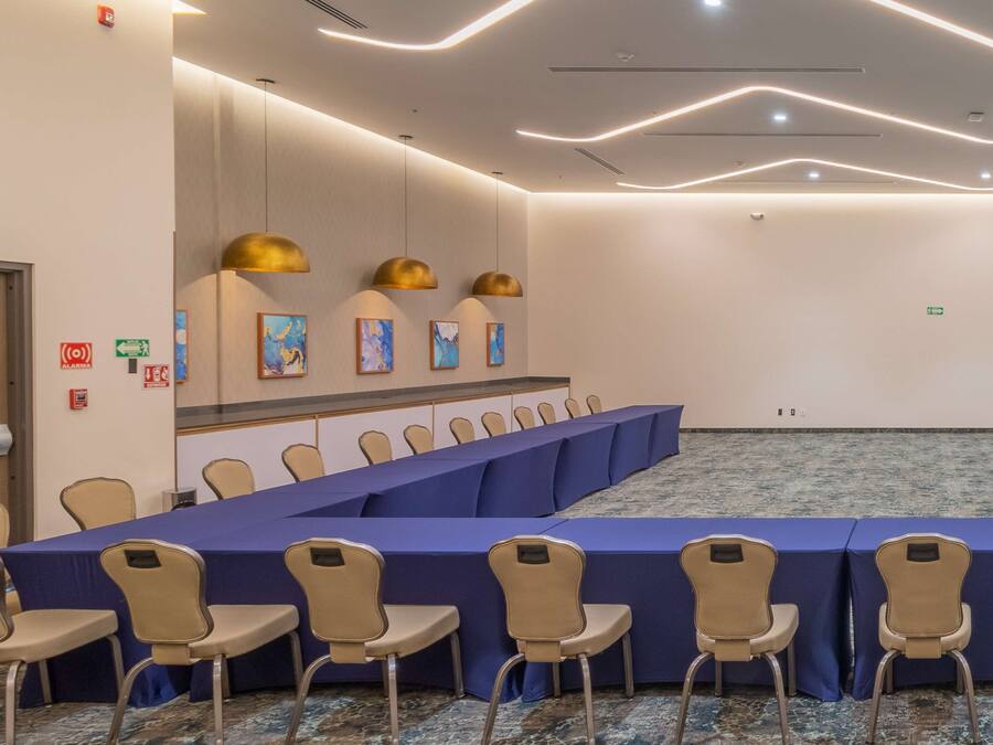Un salón de conferencias con una larga mesa, sillas color beige y manteles azules.