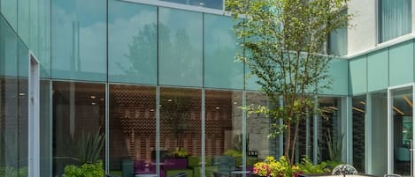 An outdoor seating area with tables and chairs, surrounded by glass walls and a building with a modern design.