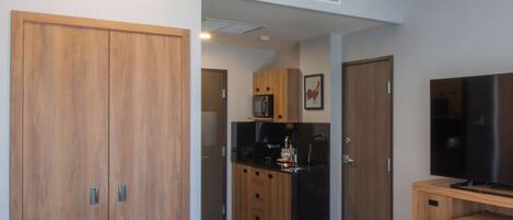 A hotel room with a bed, wardrobe, TV, and a kitchenette area.