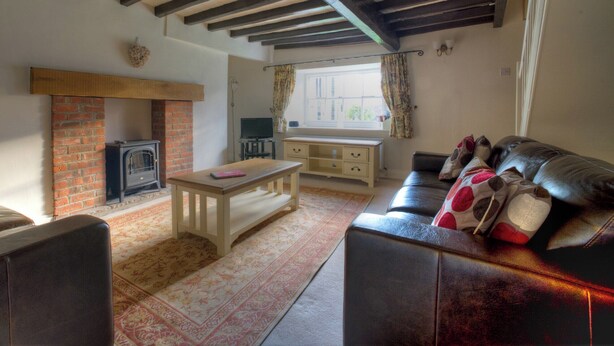 A cozy living room with exposed wooden beams, a brick fireplace, a leather sofa, and a television. - 2 bedroom accommodation in Pickering (Pickering)