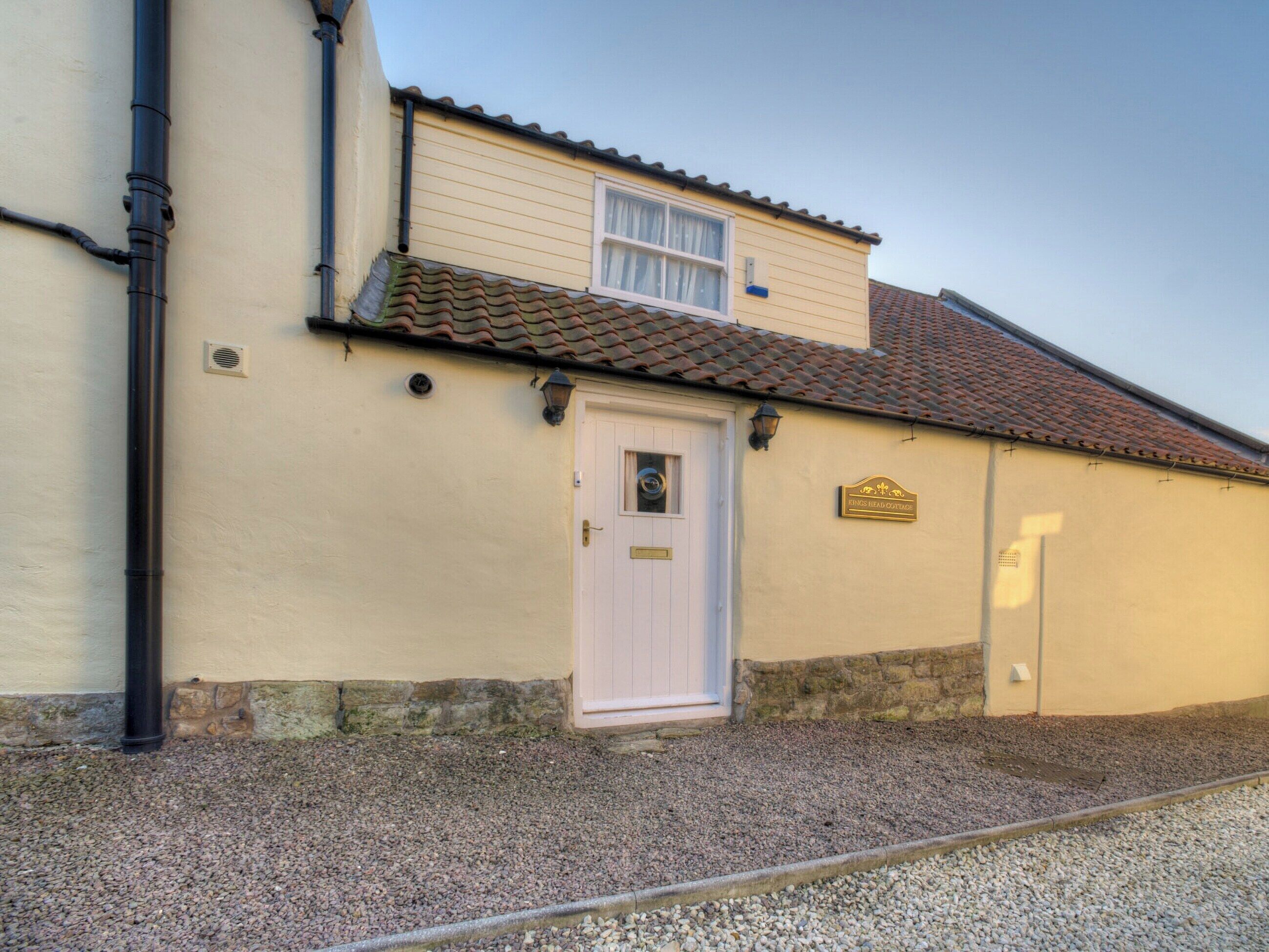 A building with a white door, a small window, and a sign that reads "Kings Head Cottage."