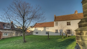 A traditional house with a tiled roof, a well-maintained lawn, and a stone wall. - 2 bedroom accommodation in Pickering (Pickering)