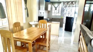 Un comedor con una mesa y sillas de madera, una cocina al fondo y piso de baldosas.