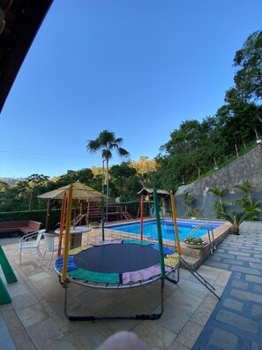 Um trampolim, uma piscina e uma estrutura de recreação de madeira em um quintal.