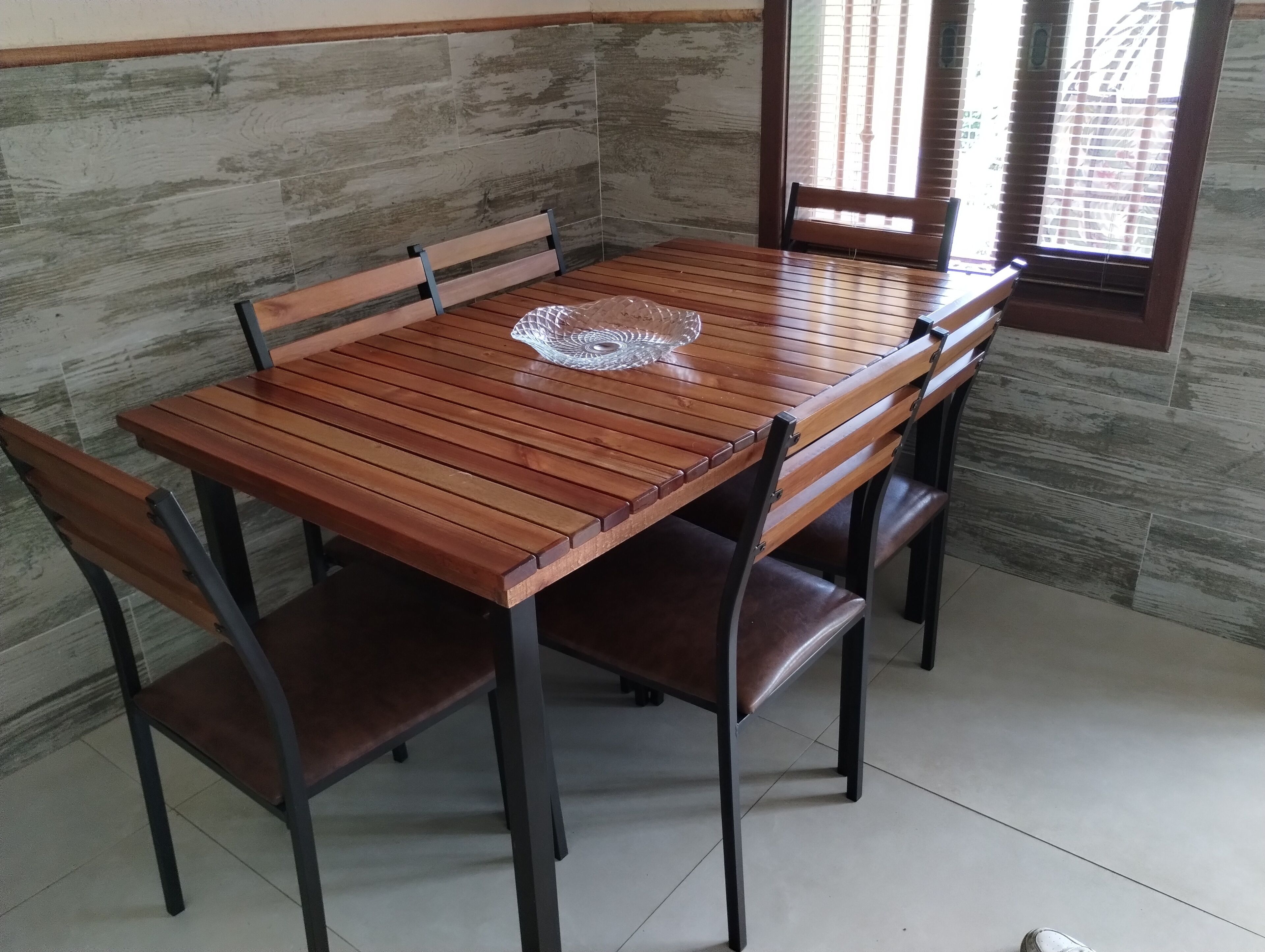 Una mesa de madera con cuatro sillas, frente a una pared de piedra con una ventana.