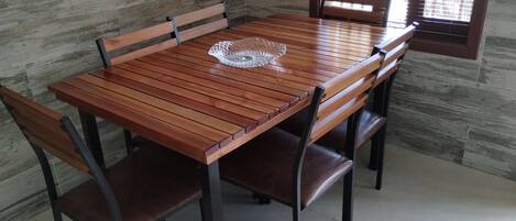 Una mesa de madera con cuatro sillas, frente a una pared de piedra con una ventana.