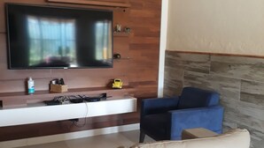 Ett modernt vardagsrum med en platt-TV som är monterad på en väggpanel av trä, en beige lädersoffa och en blå fåtölj.