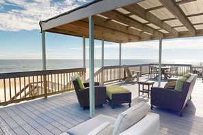 Une terrasse extérieure couverte, aménagée avec des meubles en osier et offrant une vue sur l’océan.