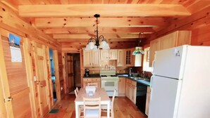 A wooden cabin with a dining area, kitchen, and a refrigerator. - Greenwood At Entangled Acres - Log Cabin w\WiFi on 16 Acre Animal Sanctuary (Owego)
