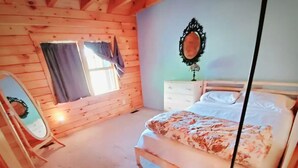 A bedroom with a wooden bed, a bedside table, a mirror, and a window with curtains. - Greenwood At Entangled Acres - Log Cabin w\WiFi on 16 Acre Animal Sanctuary (Owego)