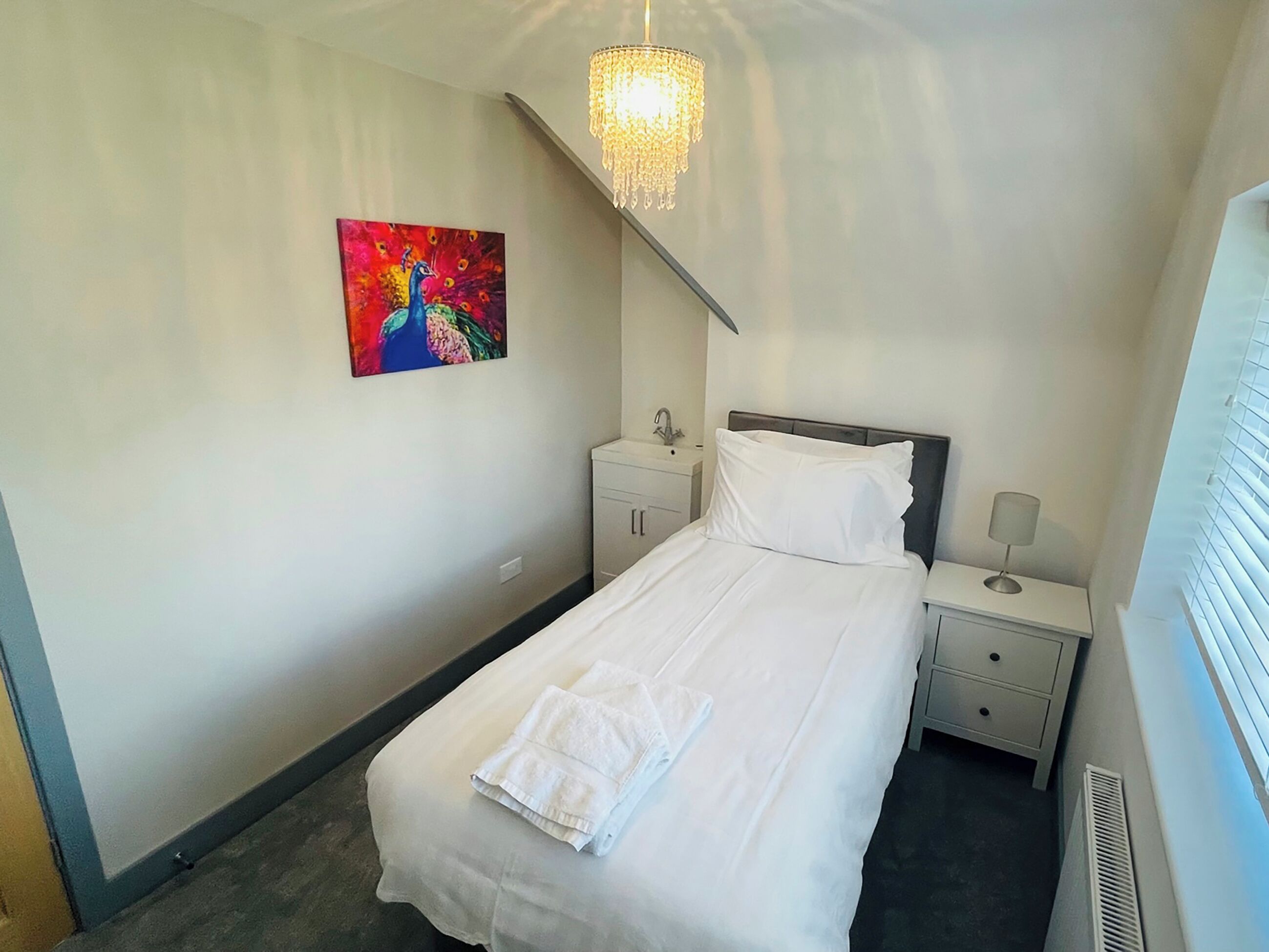 Una habitación de hotel con una cama, una mesita de noche, una lámpara, un cuadro y un candelabro.