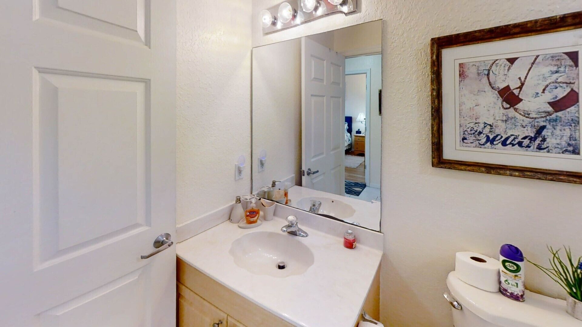 A bathroom with a white sink, a mirror, a framed artwork, and a toilet.