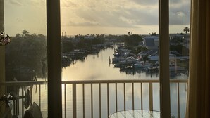 Uitzicht vanaf een balkon op een jachthaven met aangemeerde boten, een rustig wateroppervlak en woongebouwen op de achtergrond.