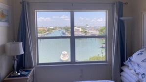 Hotelkamer met een groot raam met uitzicht op een rivier en gebouwen. Een bed met witte lakens, een nachtkastje met een lamp en een ingelijste foto aan de muur.