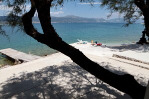 A clear view of a lake with a wooden dock leading to a beach area with lounge chairs and a small statue. - Big apt W.large Terrace&great sea View,close Beach (Trogir)
