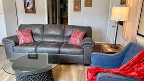 A living room with a leather sofa, a glass coffee table, and a blue armchair. There are framed pictures on the wall and a lamp on a side table. - #1 Casita Wild Mustang at the Catwalk, 2 BdRm Casita (Catron County)