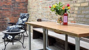 A patio area with a wooden table, a chair with a floral cushion, and a vase with flowers and a bottle. - 3 bedroom accommodation in Amble, Morpeth (Amble, Morpeth)
