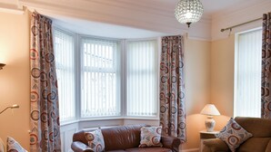 A living room with a brown leather sofa, patterned cushions, a glass coffee table, and a lamp on a side table. - 3 bedroom accommodation in Amble, Morpeth (Amble, Morpeth)