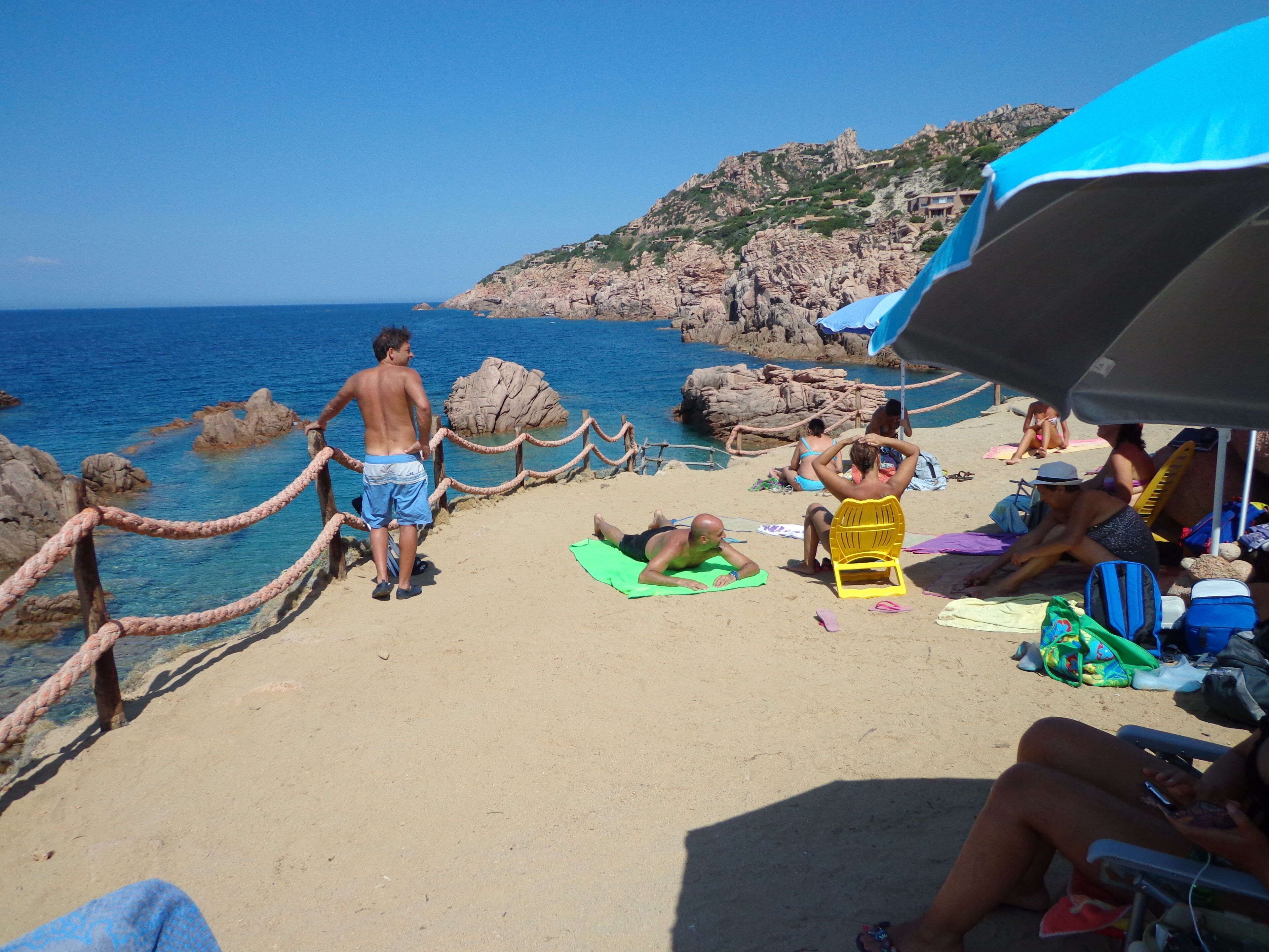 En strand med ett avspärrningsrep, folk som solar, och en bergig sluttning i bakgrunden.